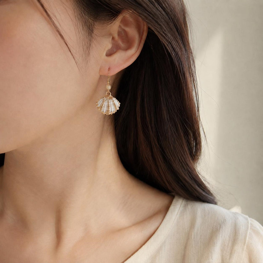 Small fan-shell earring with a gold-tone edge shown worn beside dark hair.