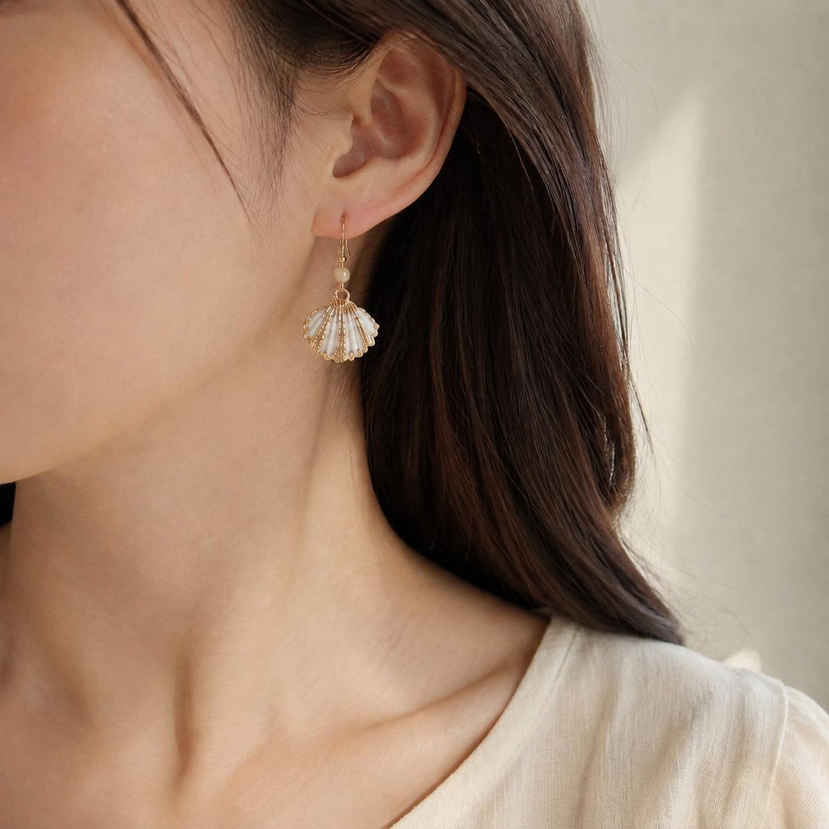 Small fan-shell earring with a gold-tone edge shown worn beside dark hair.