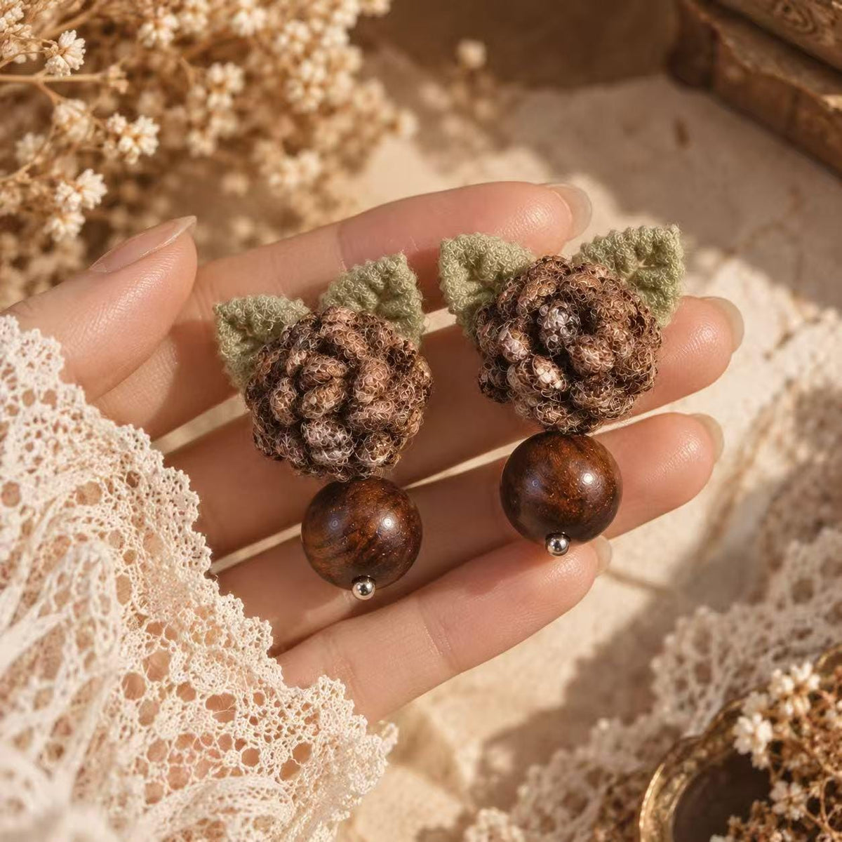 Pair of Hazelwood brown crochet-flower earrings with green leaves and bead drops held in a hand.