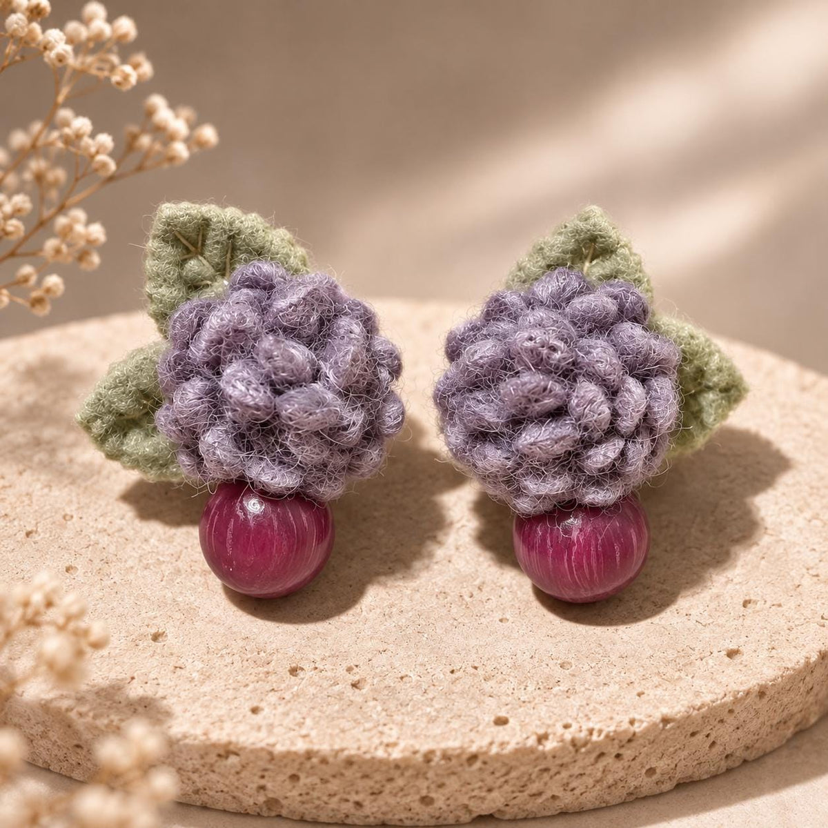 Pair of Lilac Berry crochet-flower earrings standing on a pale stone slab.