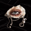 Sereine Eye LV027 — oyster-eye wearable art with smoky bronze makeup, a grey-blue gaze and pearl chain drapes